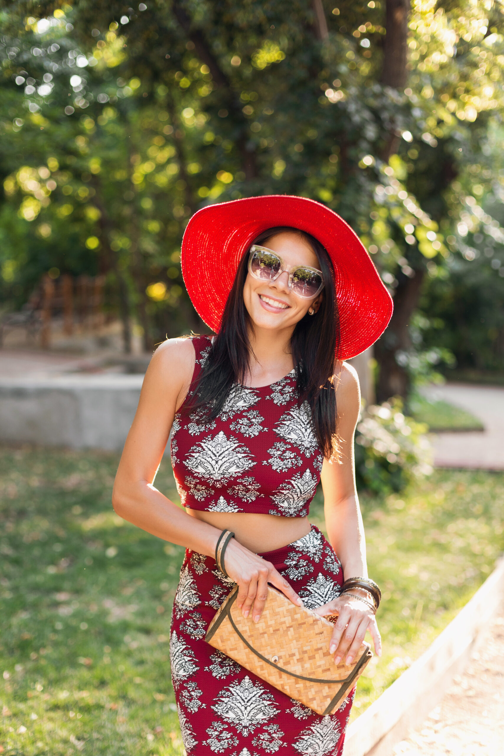 fashion portrait smiling attractive stylish woman walking park summer outfit printed dress wearing trendy accessories purse sunglasses red hat relaxing vacation scaled