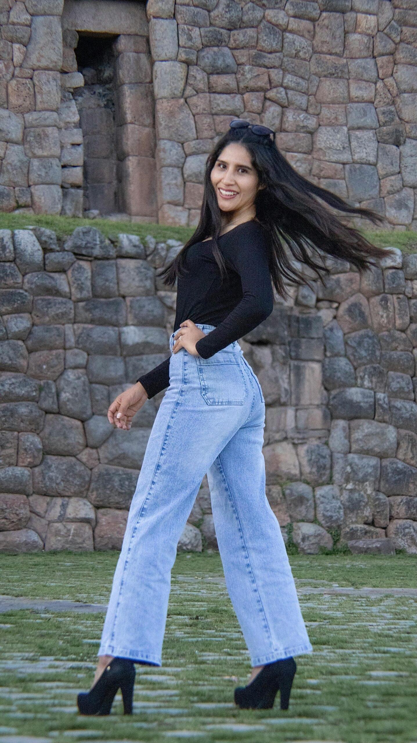 Trendy young woman poses confidently by a historic stone wall in high fashion.